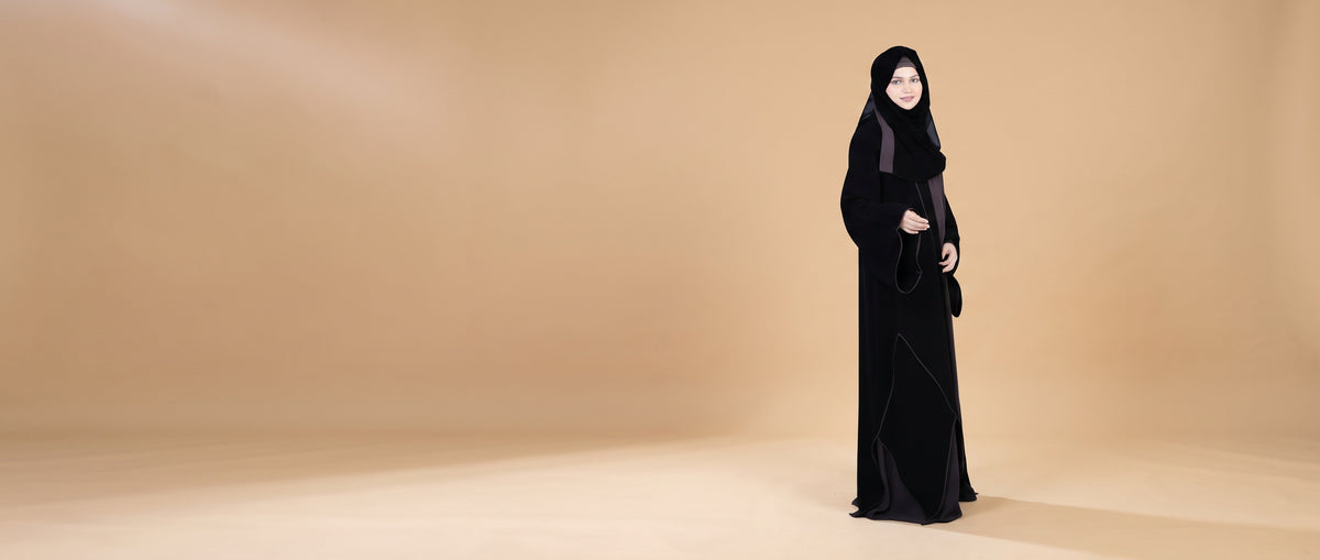 Woman wearing a full-length black Mehar Hijab abaya against a warm studio backdrop